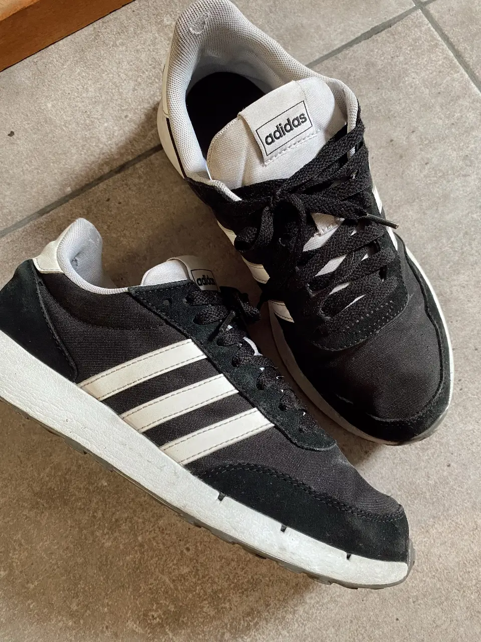 Zapatillas Adidas negras con detalles blancos. Diseño clásico con las tres tiras icónicas de la marca. 