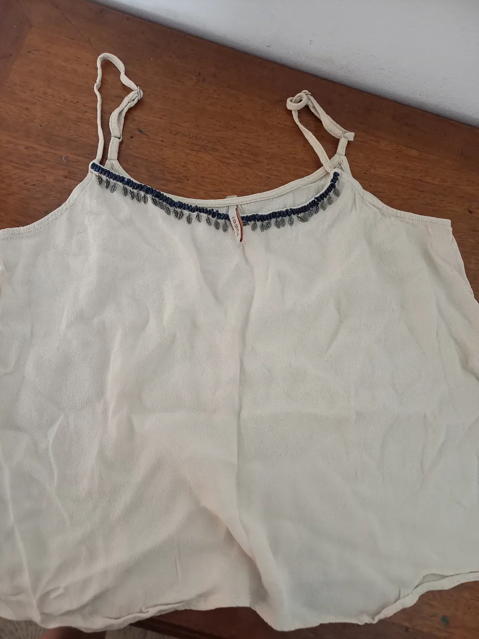 Musculosa de tela liviana color crudo, con detalles de canutillos y flecos en el escote. Ideal para un look fresco y bohemio.