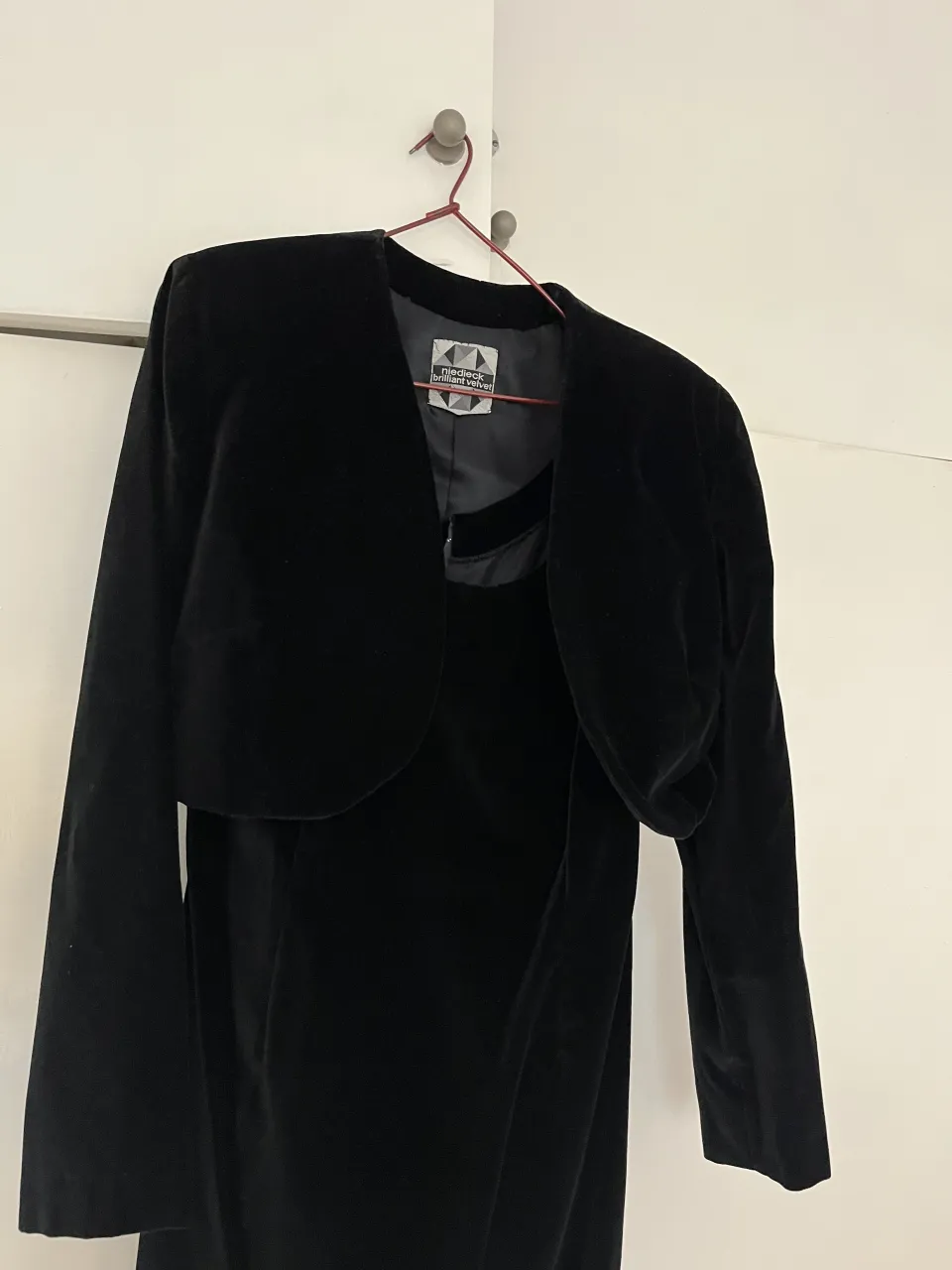 Vestido negro de terciopelo con saco corto haciendo juego. El vestido es sin mangas y tiene un escote en V. El saco es corto, con mangas largas y cuello redondo.