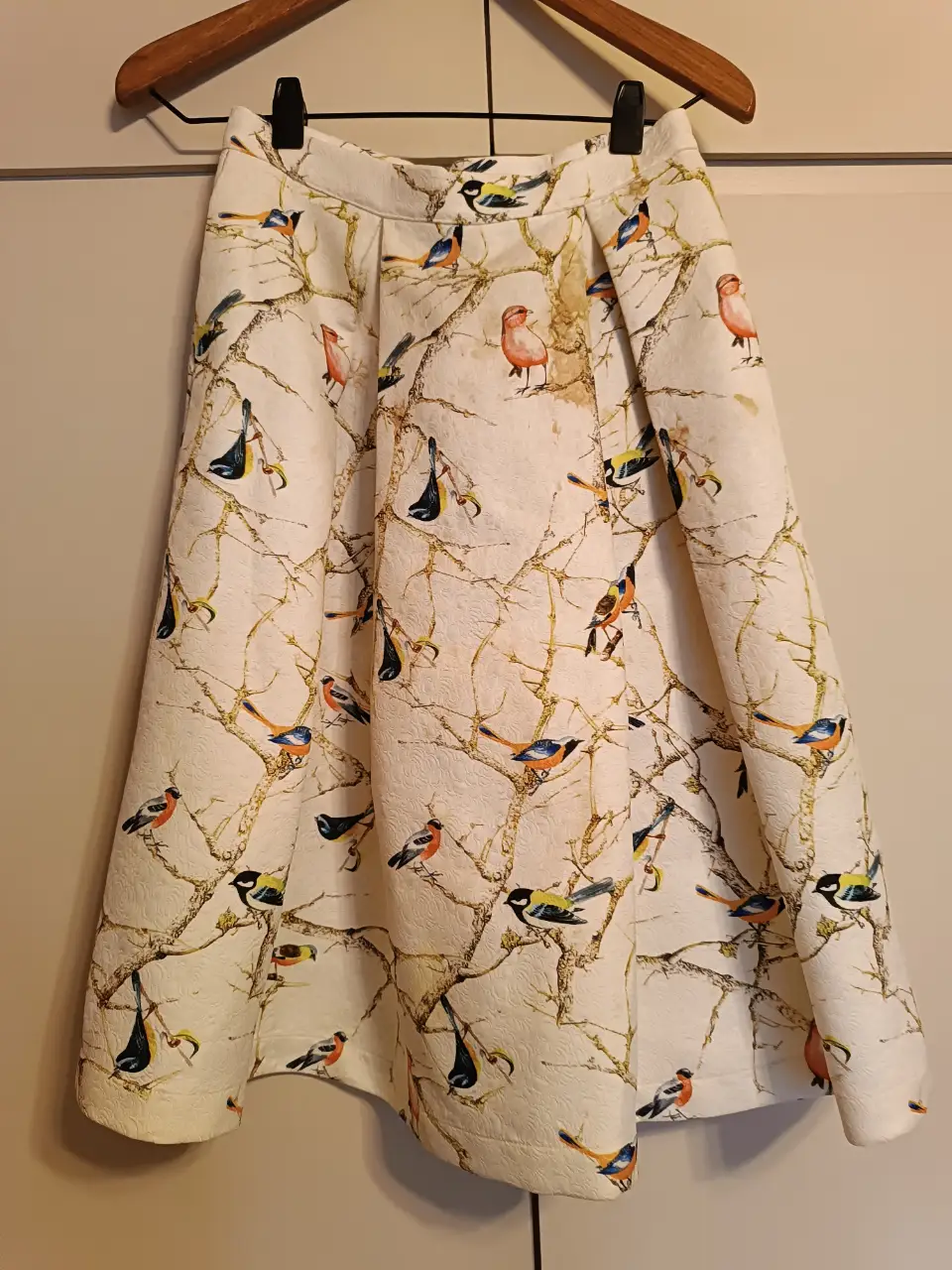 Pollera midi con estampado de pájaros y ramas sobre fondo blanco. Tiene cierre y ganchos en la cintura. Ideal para un look casual y con estilo.