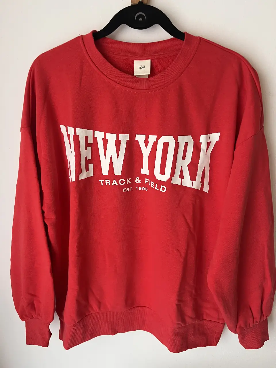 Buzo de cuello redondo rojo con estampado "NEW YORK TRACK & FIELD EST. 1990" en blanco. Ideal para un look casual y urbano.marca HyM, sin uso.