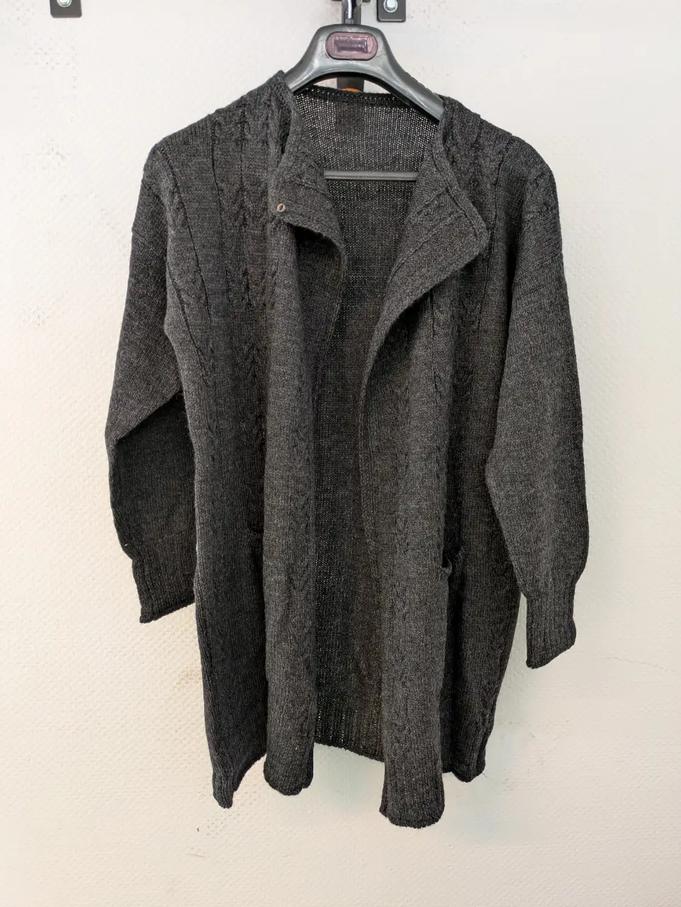 Cardigan largo de tejido grueso en color gris oscuro. Posee mangas largas y dos bolsillos delanteros. Ideal para un look casual y abrigado.