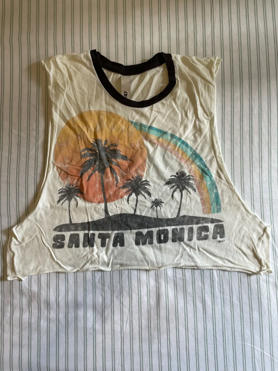 Musculosa amarilla con estampa de palmeras, sol y arcoíris en el frente. La estampa dice "SANTA MONICA". Tiene cuello y mangas con borde negro.