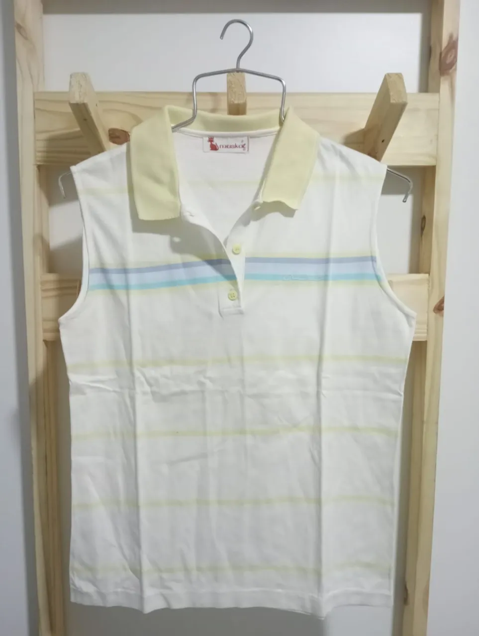 Conjunto de remera polo sin mangas y shorts. La remera es blanca con finas rayas horizontales en celeste, verde y amarillo, cuello polo y botones. El short es de color amarillo pálido, con bolsillos laterales y un corte clásico.