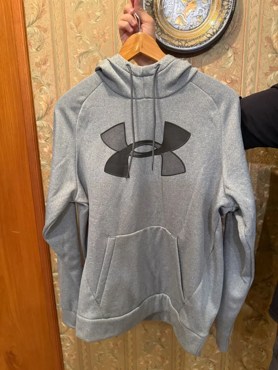 Buzo canguro gris de hombre con el logo de Under Armour en negro. Ideal para usar en actividades deportivas o para un look casual.