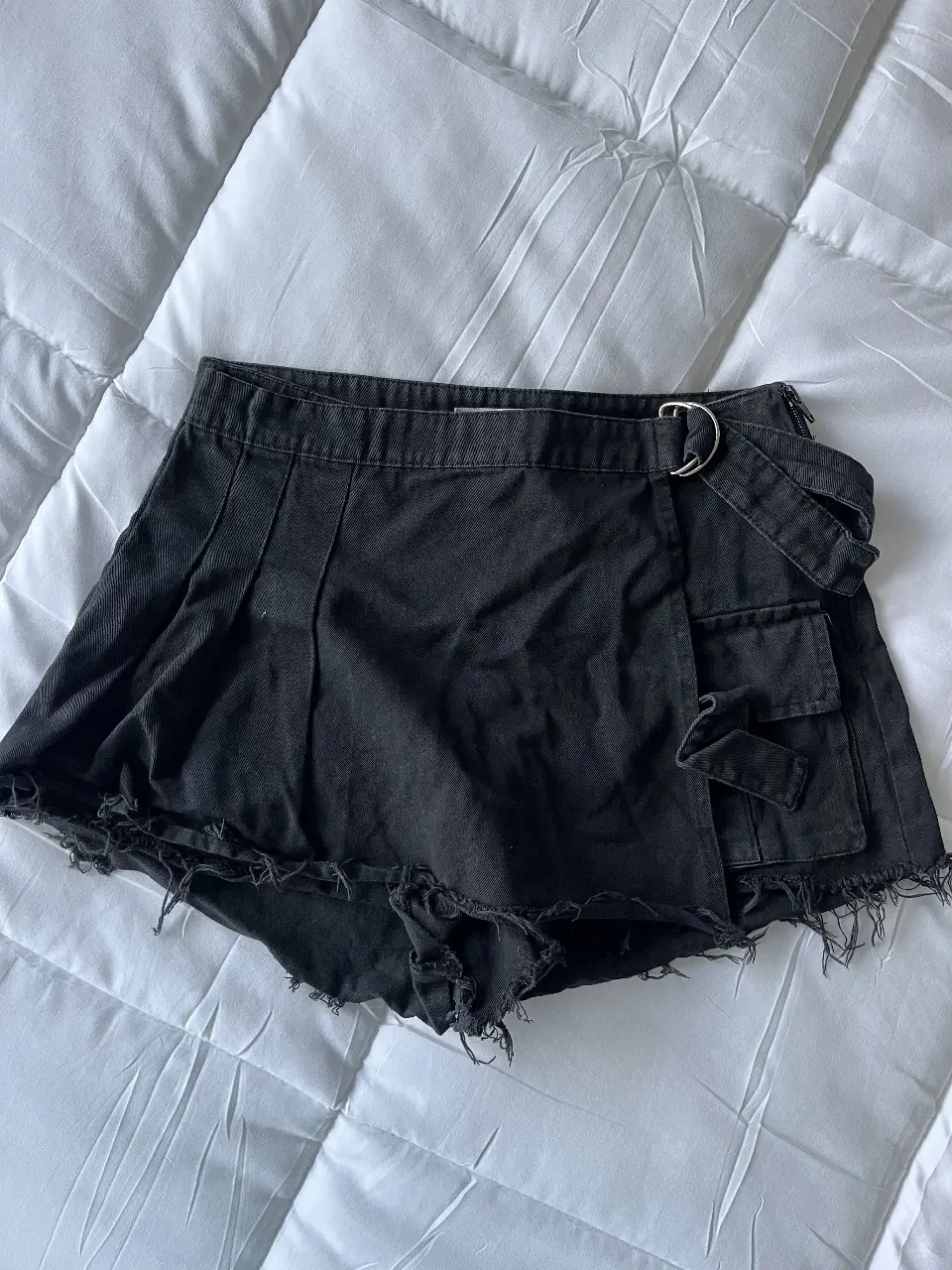 Short pollera de jean negro con detalles de corte desflecado y diseño utilitario. Cuenta con bolsillos cargo y un cinturón con hebilla metálica. Talle 36