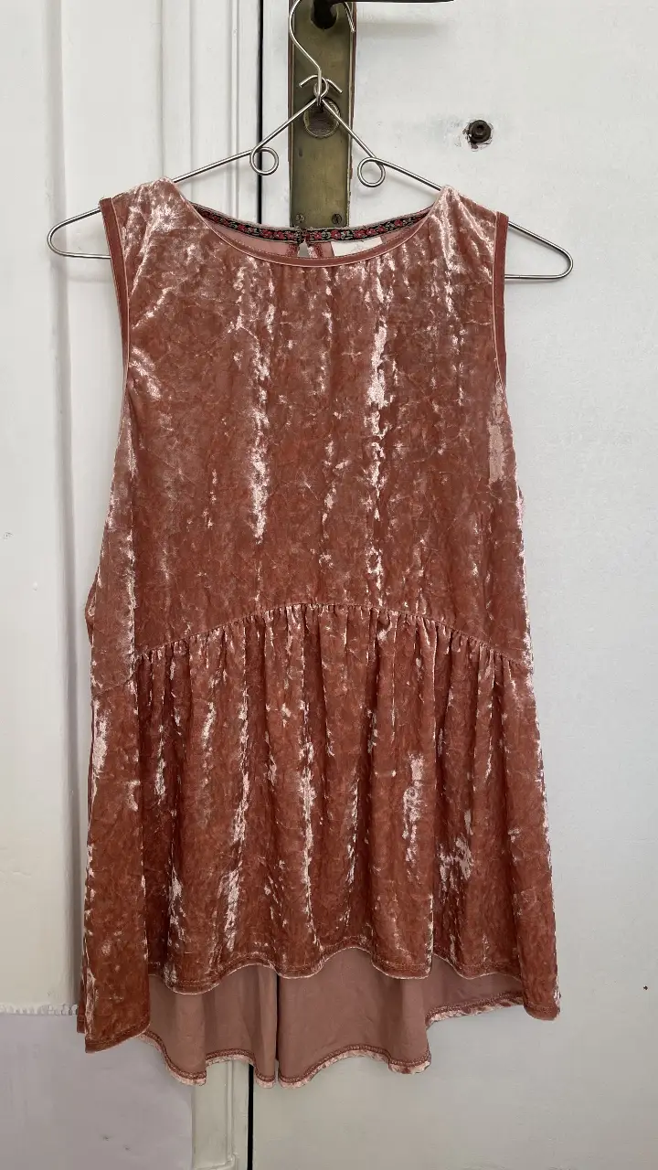 Blusa de terciopelo rosa, sin mangas, con detalle de volado en la cintura. Ideal para un look elegante y cómodo.