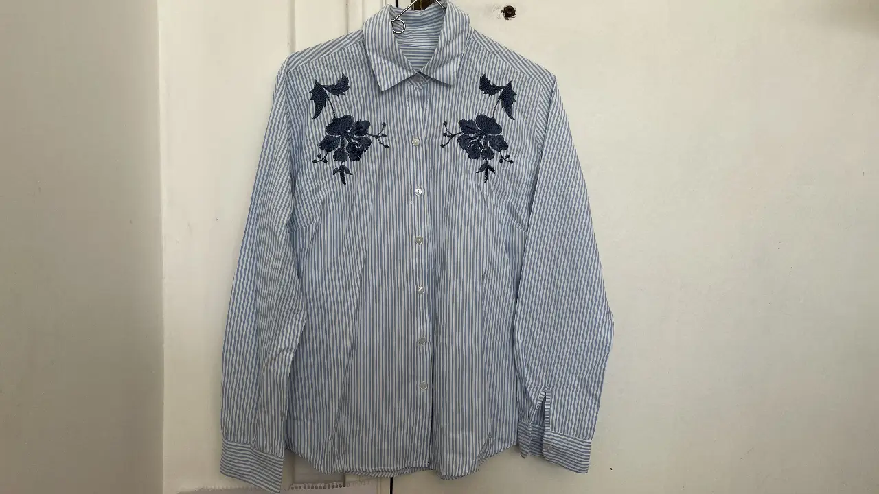Camisa a rayas celeste y blanca con bordado floral en el pecho. Ideal para un look casual y fresco.
