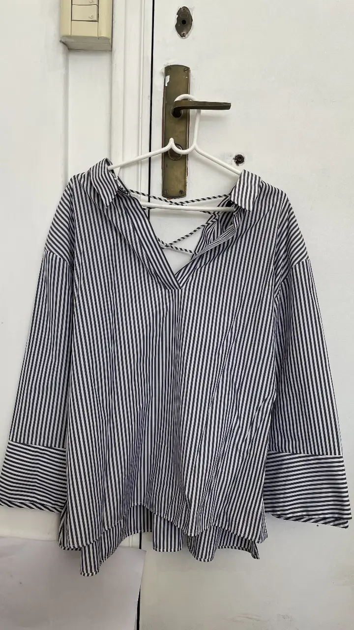 Blusa a rayas verticales en blanco y azul marino, con detalle de espalda cruzada y puños con botones. Ideal para un look casual y moderno.
