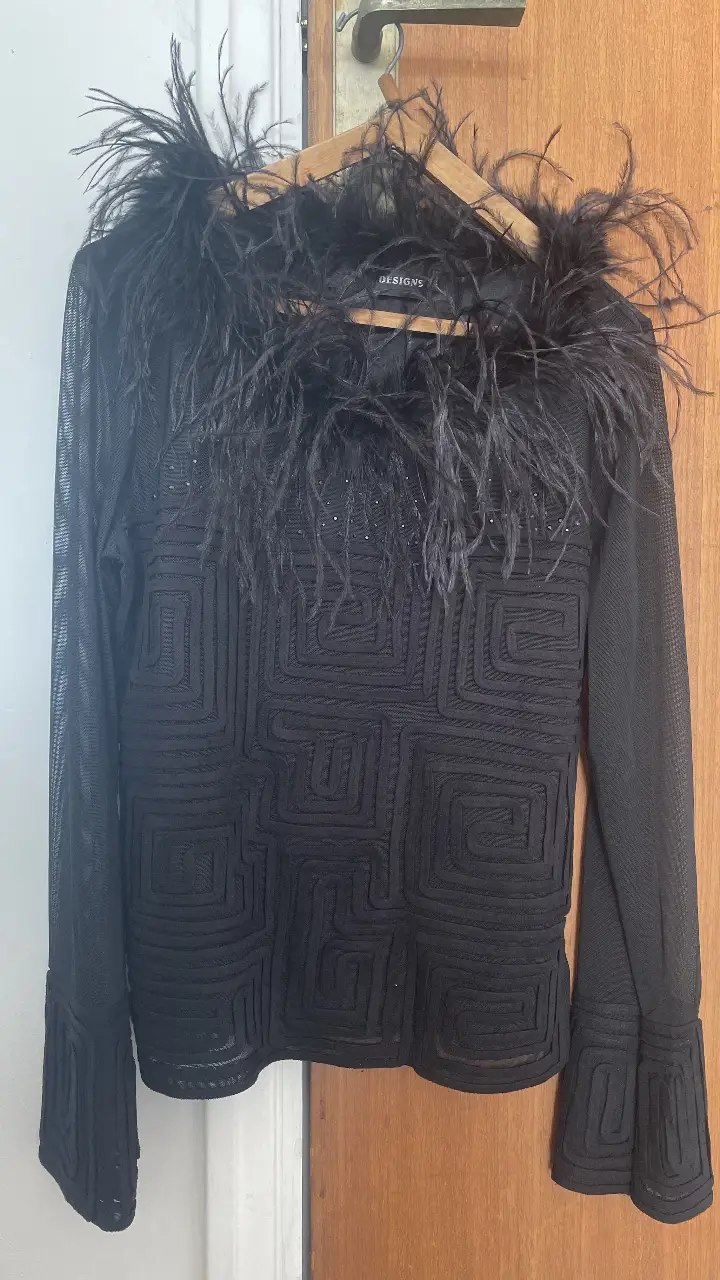 Blusa negra con detalle de plumas en el cuello y diseño geométrico en relieve. Ideal para eventos especiales o salidas nocturnas.