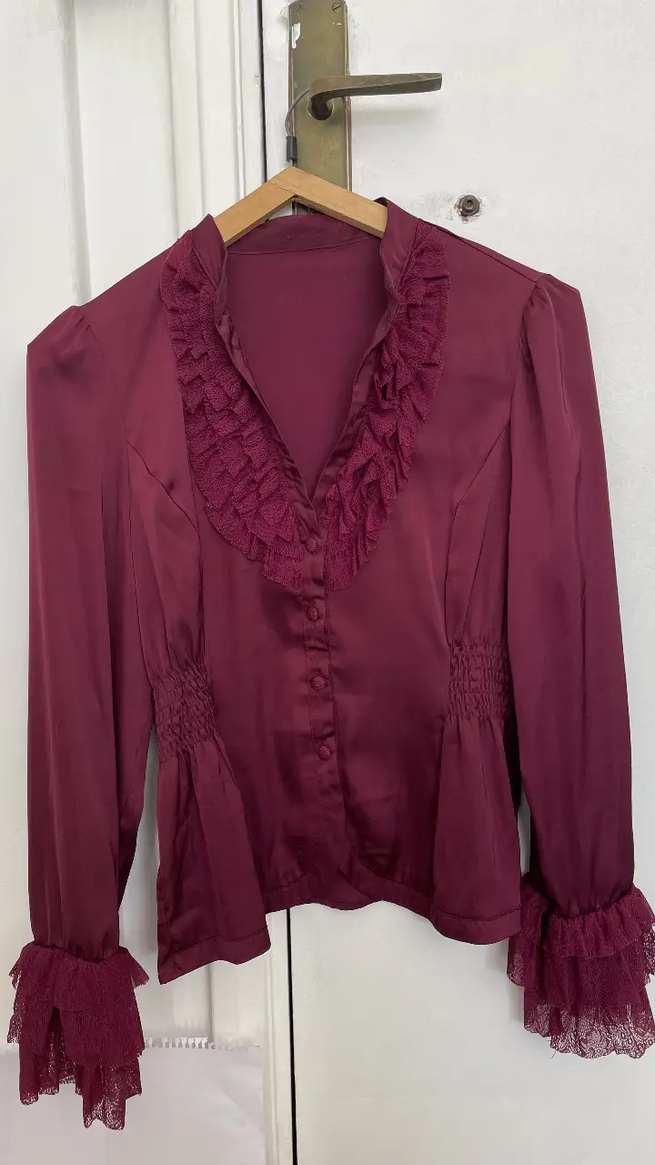 Blusa de manga larga color borgoña con detalles de encaje en los puños y cuello. Diseño elegante con frunces en la cintura y botones frontales.