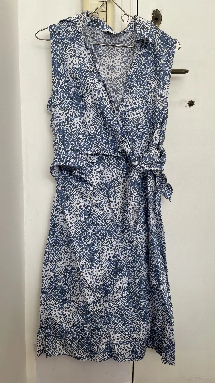 Vestido midi de mujer, con estampado de diseño en tonos azules y blancos. Corte envolvente con lazo en la cintura, sin mangas y cuello camisero. Ideal para un look fresco y elegante.