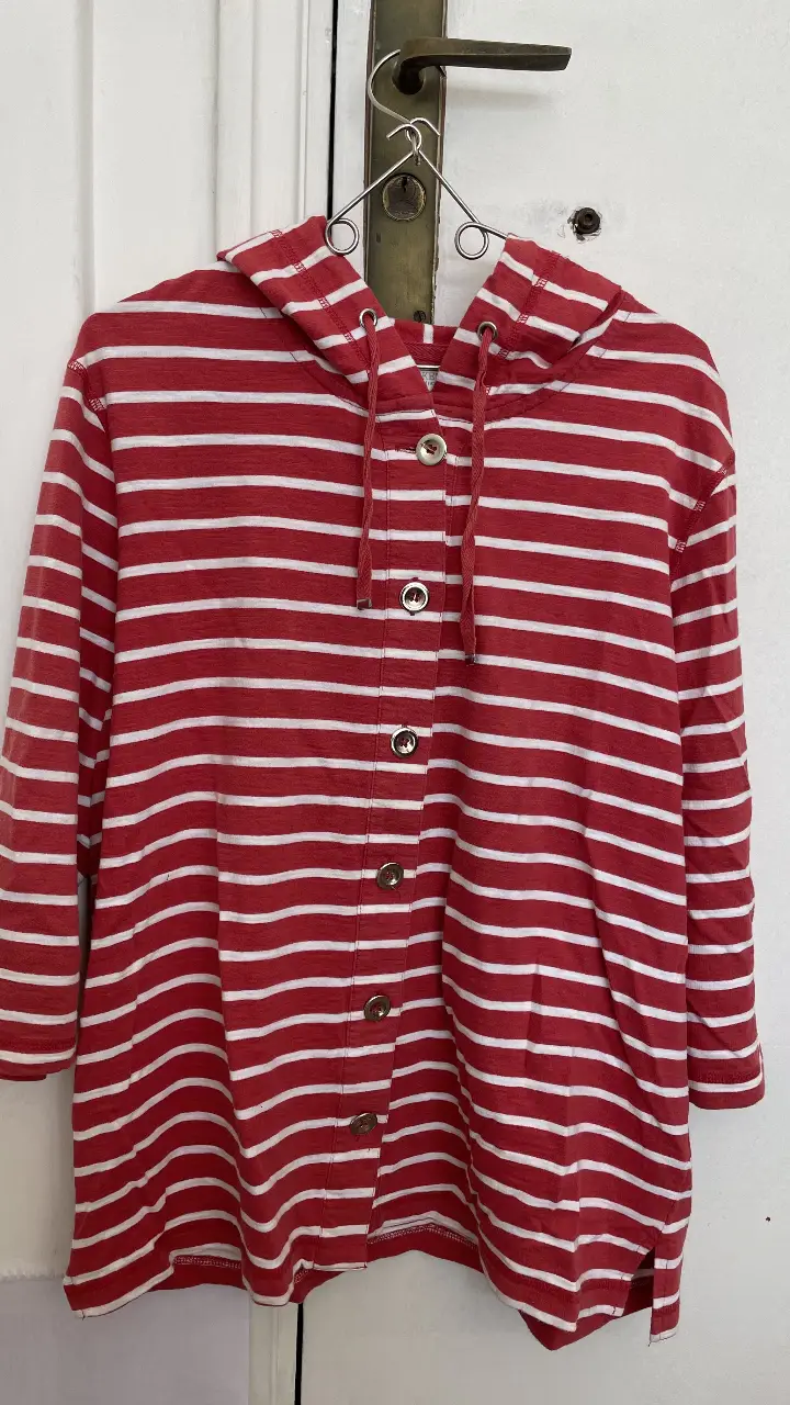 Buzo con capucha a rayas rojas y blancas, con botones y mangas 3/4. Ideal para un look casual y cómodo. 100% algodón.