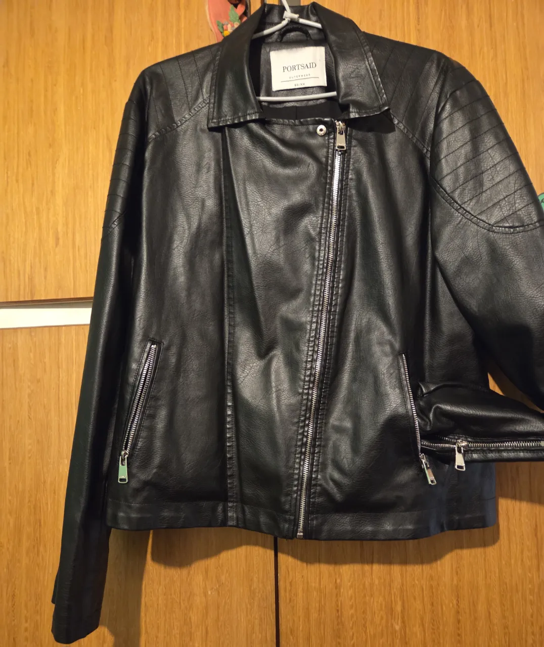 Chaqueta de cuero sintético negra estilo biker para mujer. Con cierre frontal, bolsillos con cremallera y detalles acolchados en los hombros. Ideal para un look moderno y versátil.