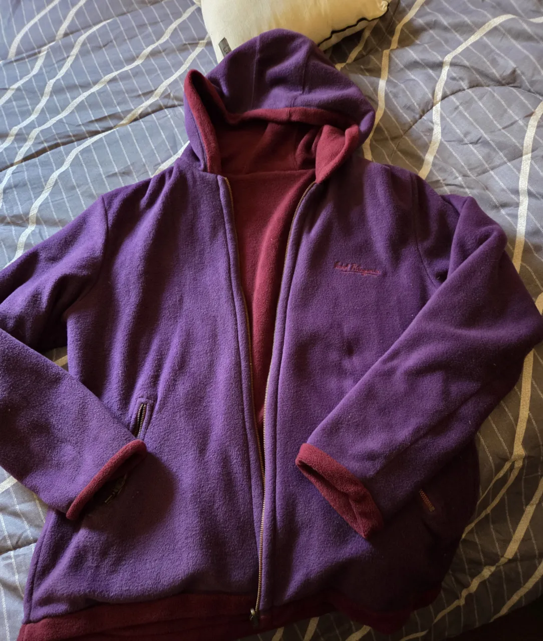 Buzo con cierre reversible, de polar, con capucha. Un lado es violeta y el otro rojo. Tiene el logo de la marca bordado en el pecho.