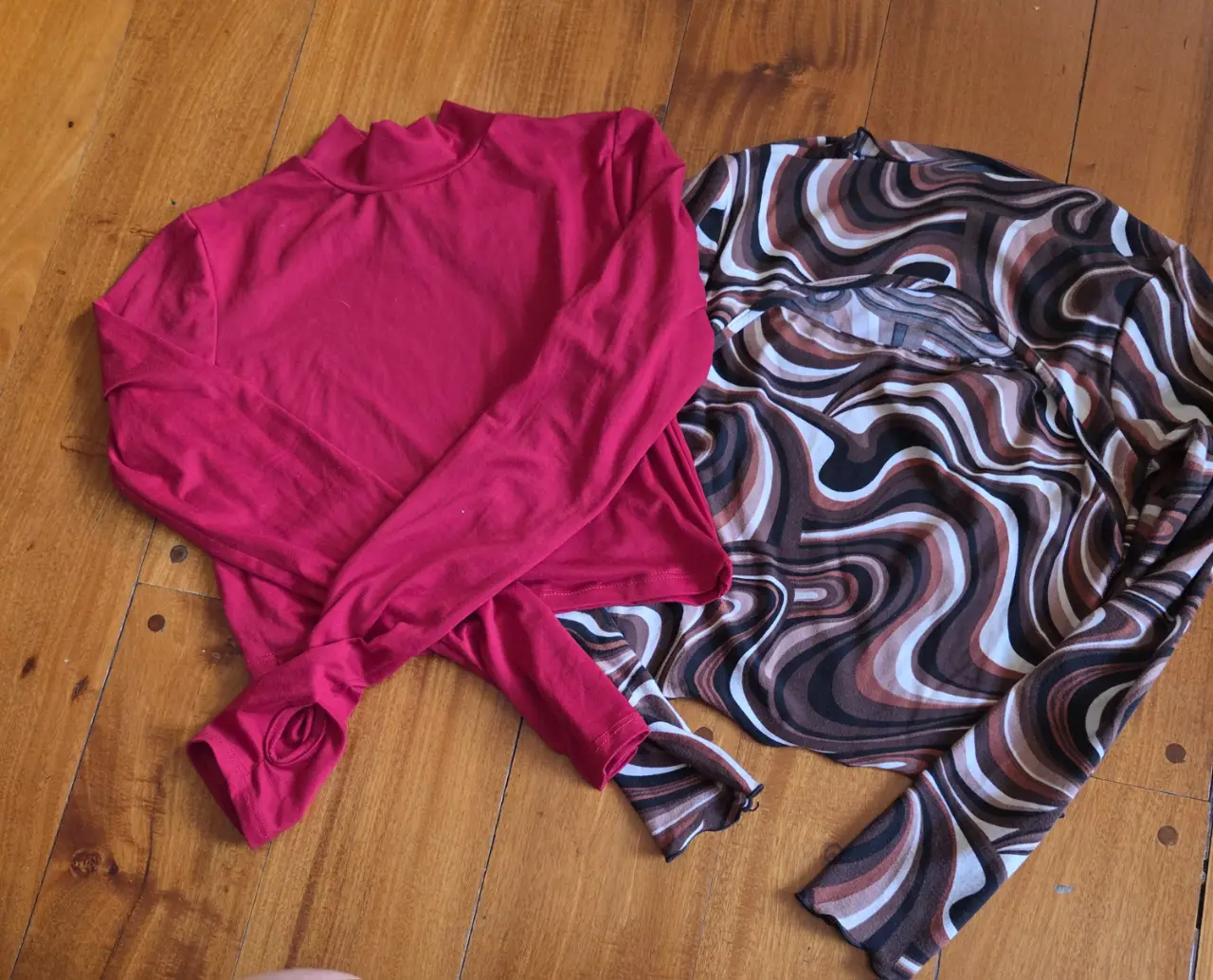 Remera manga larga de cuello alto en color rojo con detalles para el dedo pulgar. La otra remera es de manga larga con estampado psicodélico en tonos marrones.