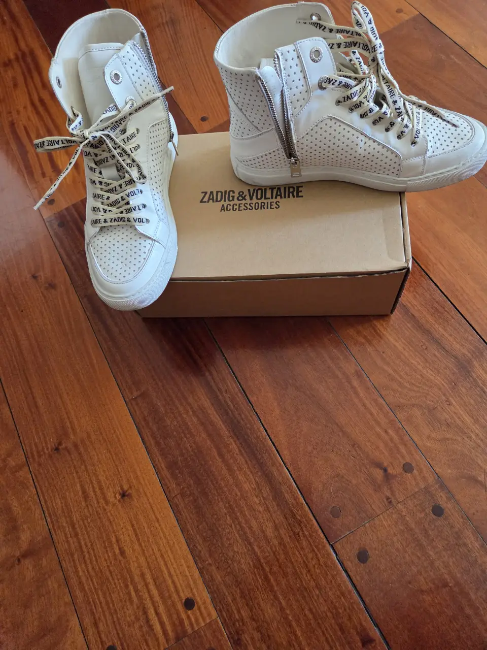 Zapatillas Zadig & Voltaire blancas de caña alta con detalles perforados y cierre lateral. Cordones con logo de la marca. Ideales para un look casual y moderno.