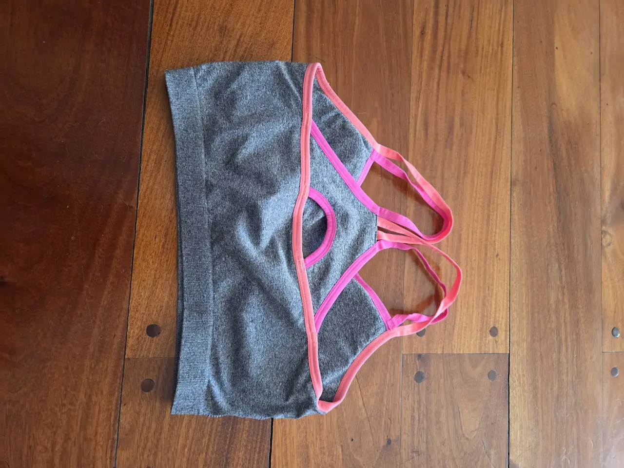 Top deportivo gris con detalles en rosa. Ideal para entrenamientos de alto impacto. Diseño sin costuras para mayor comodidad y libertad de movimiento. Perfecto para combinar con calzas o shorts deportivos.