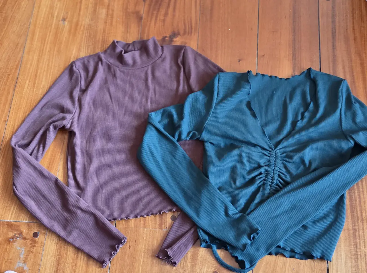 Remeras manga larga de tejido acanalado, una en color marrón con cuello alto y otra verde con escote en V y fruncido. Ambas con terminación ondulada en el borde.