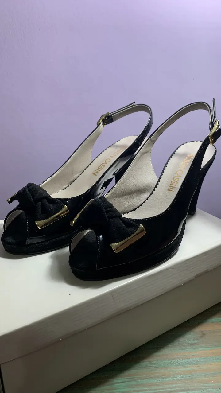Sandalias de taco alto negras de charol con moño de gamuza y detalle dorado. Marca Ruben Cassin. Taco de 8 cm