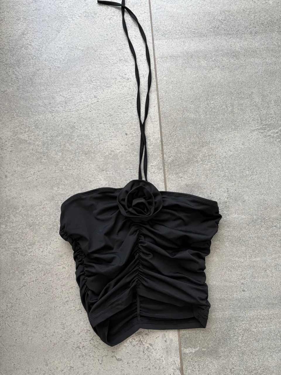 Top negro con tiras finas y detalle de flor en el busto. Posee fruncido en la parte delantera.