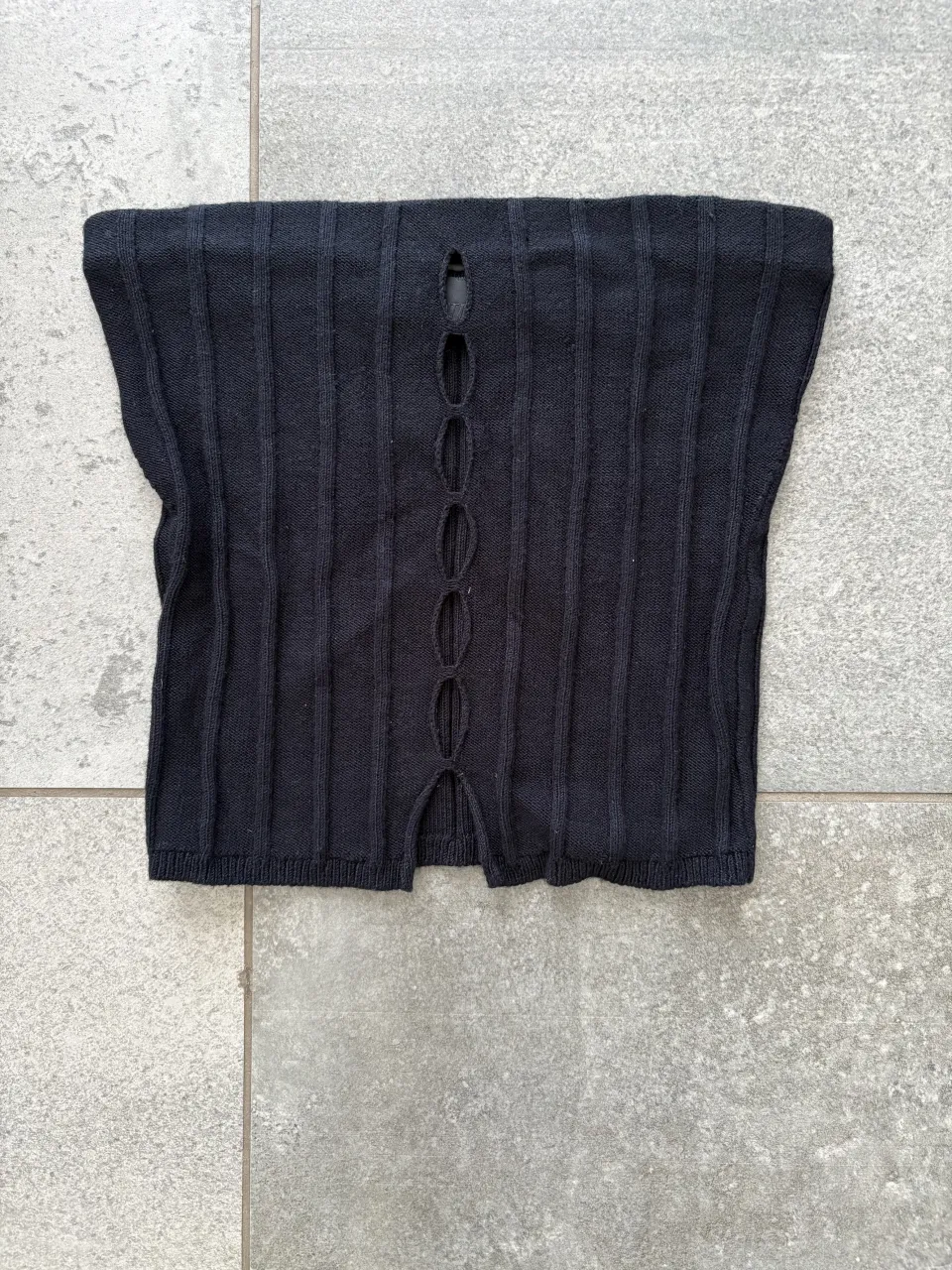 Top negro de tejido acanalado con detalles de recortes frontales y aberturas verticales.