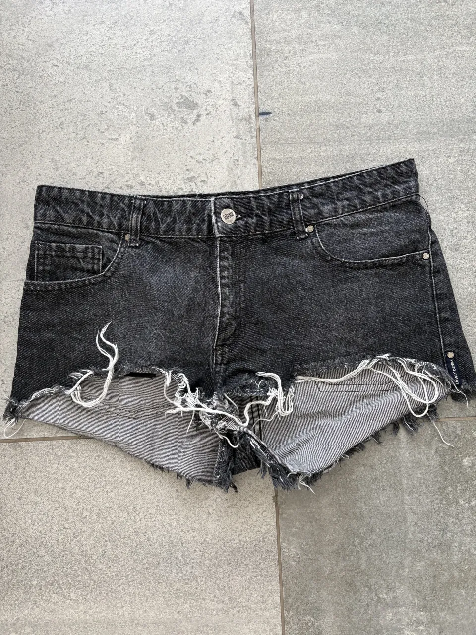 Shorts de jean negros con roturas y detalles deshilachados en el borde inferior.