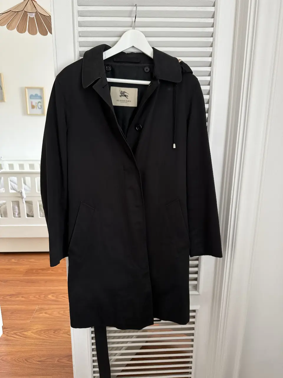 Trench coat negro de la marca Burberry, con capucha y cinturón. Ideal para lluvia y ocasiones formales.