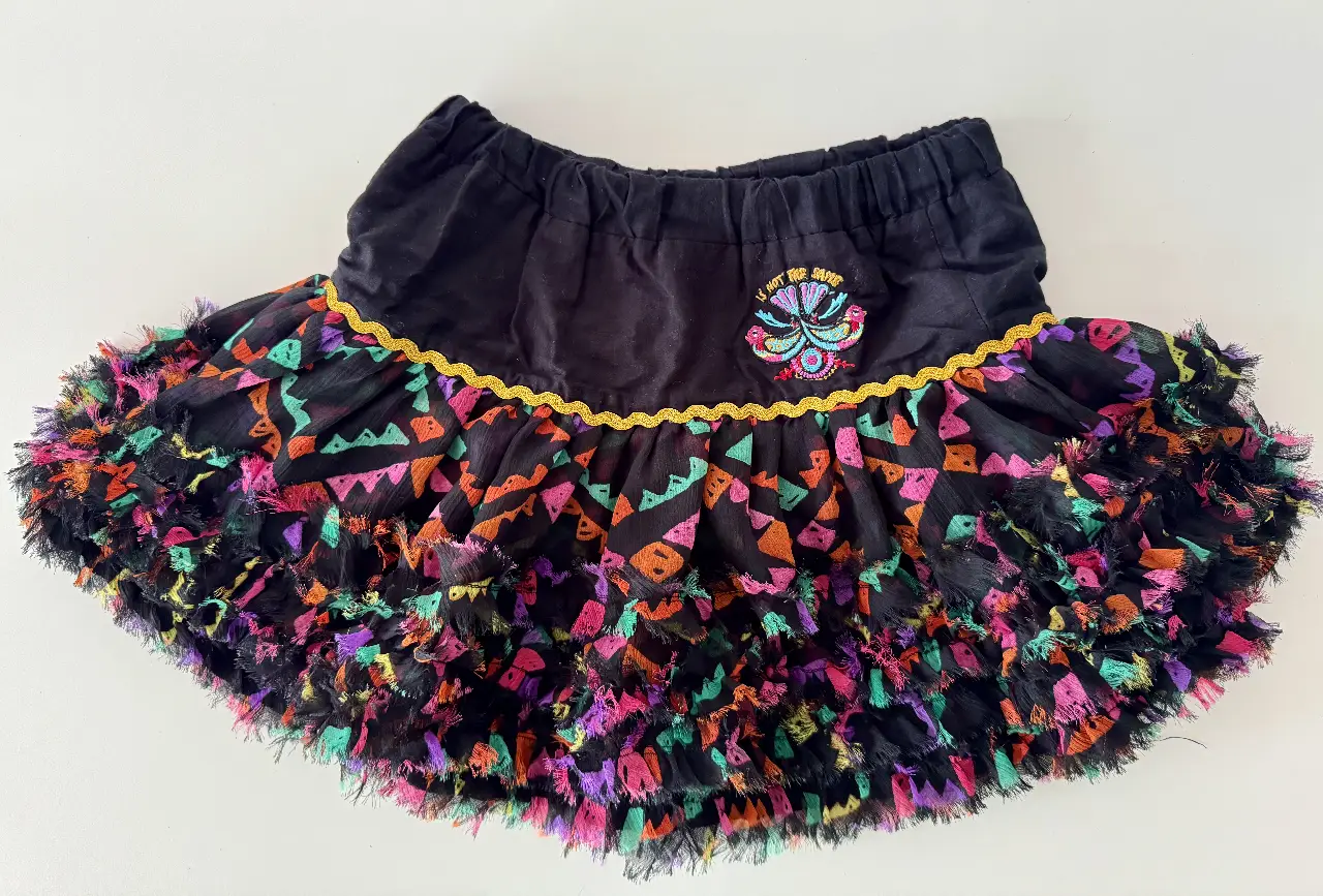 Pollera larga de niña, con cintura elastizada negra y volados con detalles coloridos. Diseño con bordado y detalles dorados. Ideal para un look festivo y original.