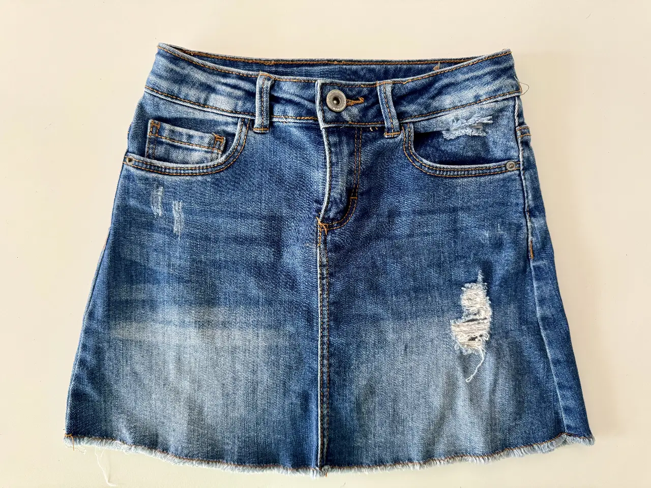 Minifalda de jean azul con detalles de roturas y desgaste. Ideal para un look casual y moderno.