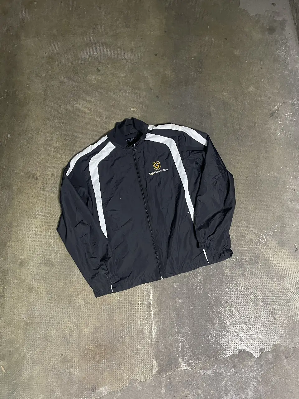 Campera deportiva negra de Amazon Fulfillment con detalles en blanco. Ideal para actividades al aire libre o uso casual. Con cierre frontal y logo de la marca.