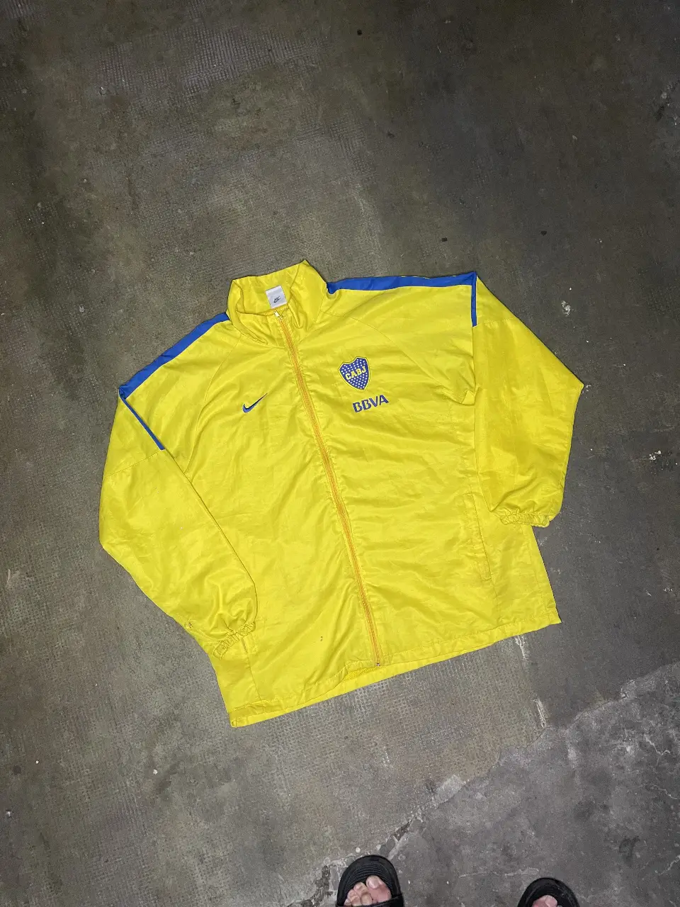 Campera rompevientos amarilla del Club Atlético Boca Juniors, con detalles en azul. Con logo de Nike y escudo del club. Talle XXL.