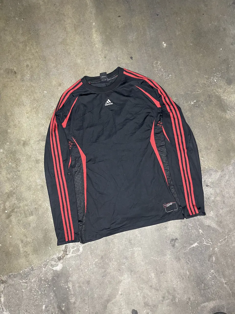 Remera manga larga Adidas Team Signature Tracy McGrady Edition, negra con detalles rojos y las tres tiras características de la marca en las mangas. Ideal para entrenar o para un look deportivo.