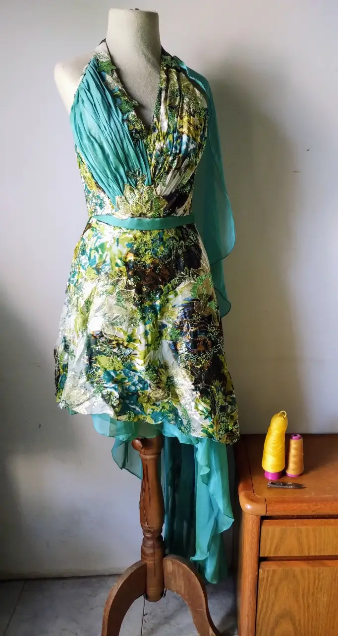 Vestido largo de fiesta con estampado floral en tonos verdes y dorados. Diseño halter con detalles plisados y falda con vuelo. Ideal para eventos especiales.