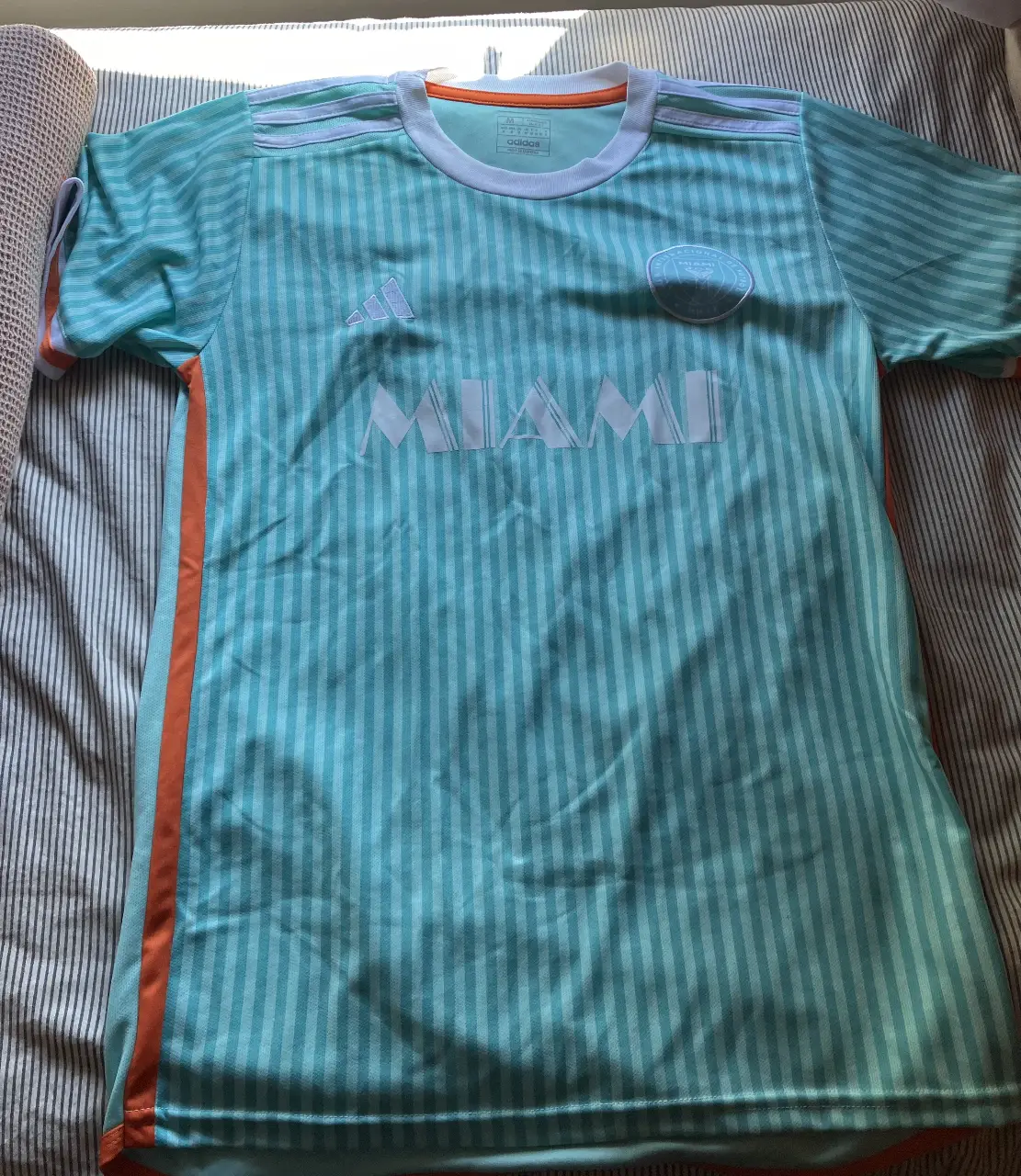 Camiseta de fútbol del Inter de Miami, con el número 10 y el nombre de Messi en la espalda. Diseño a rayas celeste y naranja, con el logo de Adidas y el escudo del equipo.