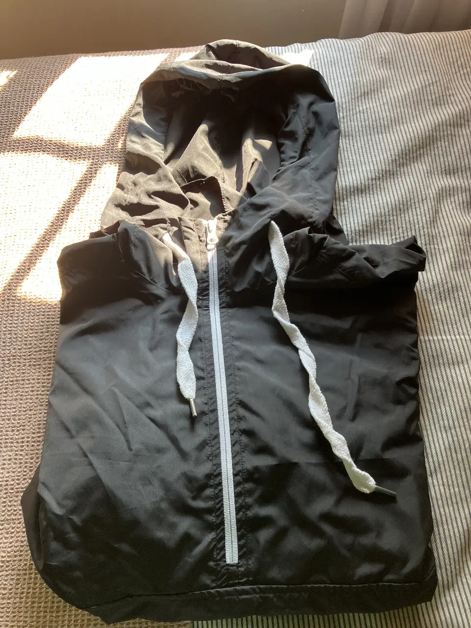 Anorak rompevientos negra con capucha y cierre 3/4 blanco. Ideal para actividades deportivas o uso casual en días de lluvia.