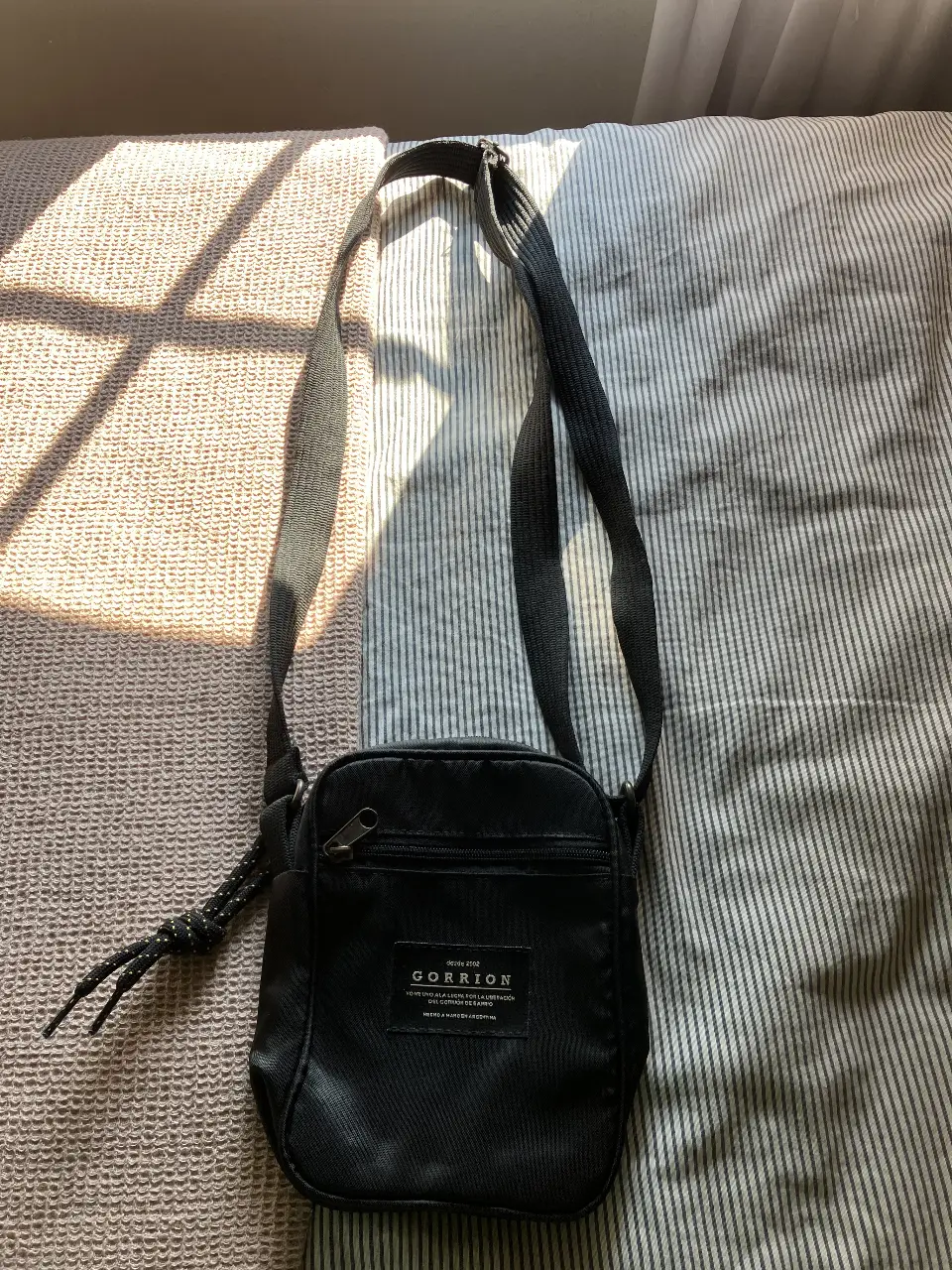 Bandolera negra, ideal para llevar lo esencial. Confeccionada en material resistente, cuenta con un compartimento principal y un bolsillo frontal con cierre.