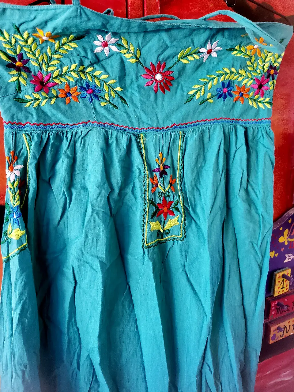 Vestido largo de algodón con bordados florales en tonos vibrantes. Diseño artesanal con detalles en el pecho y mangas, ideal para un look bohemio y fresco.