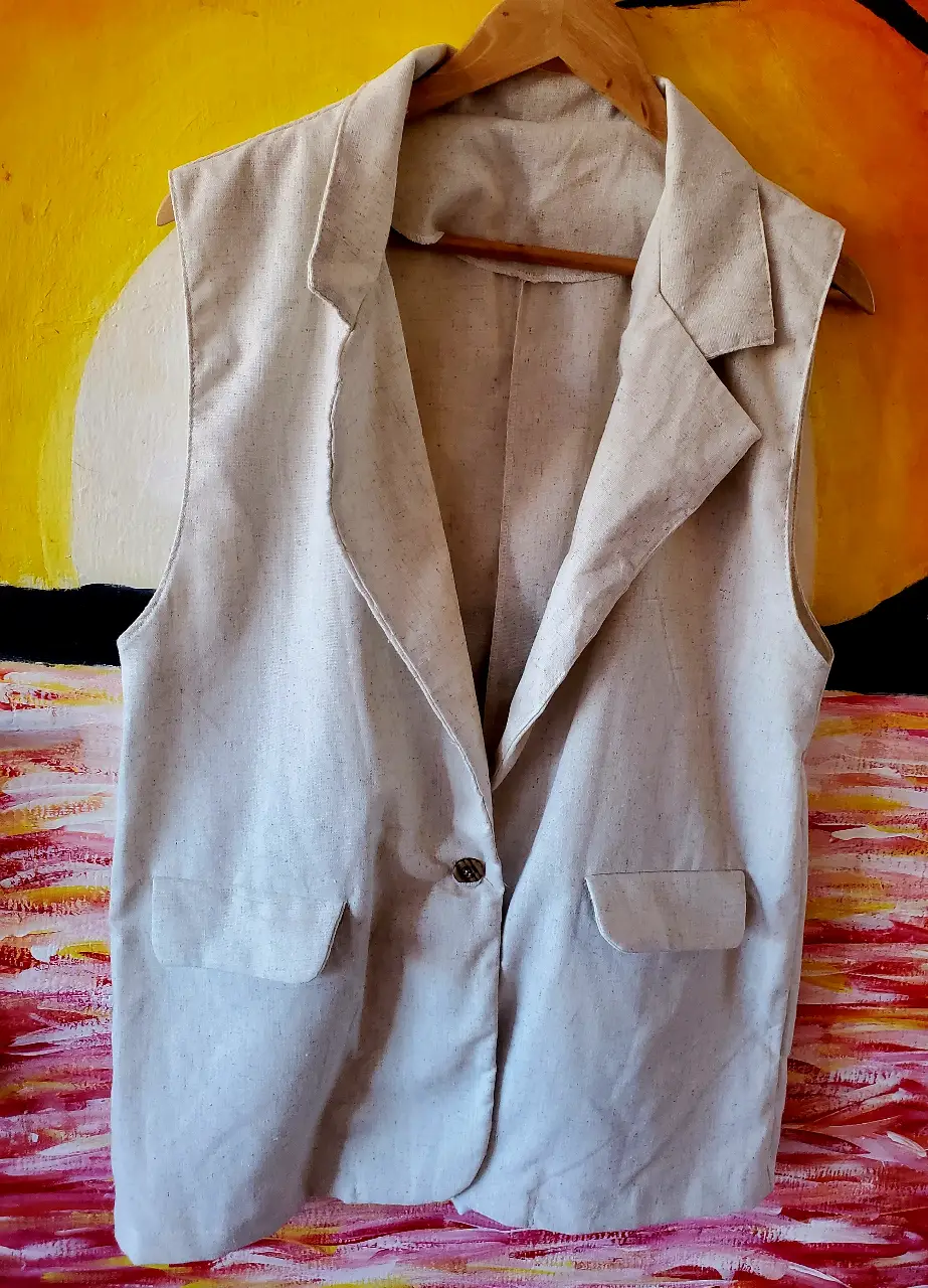 Chaleco sastrero de lino color crudo, ideal para un look elegante y fresco. Confeccionado en lino, este chaleco sin mangas presenta un diseño clásico con solapas y bolsillos delanteros. Perfecto para combinar con camisas o blusas, agregando un toque sofisticado a cualquier outfit.