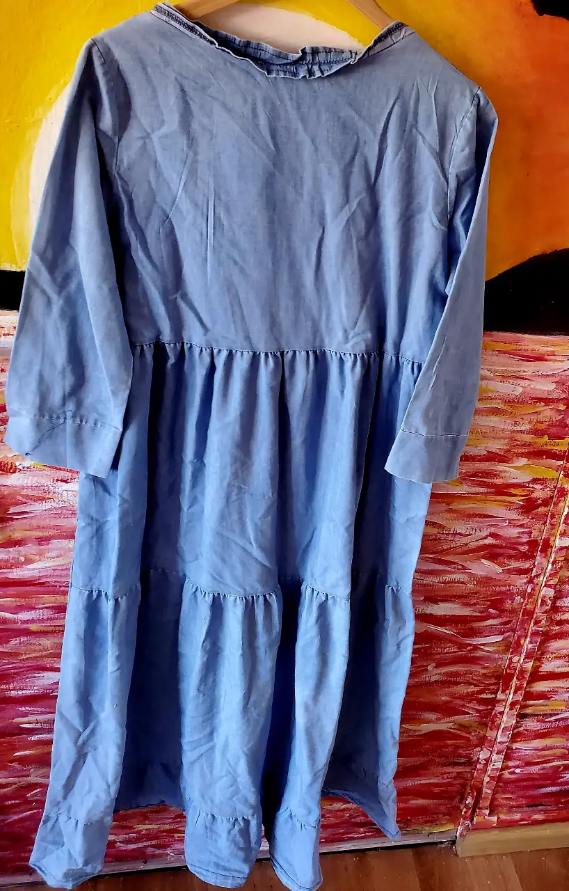 Vestido midi de jean azul claro, con mangas 3/4 y detalles de volados en el cuello y la falda. Ideal para un look casual y fresco.
