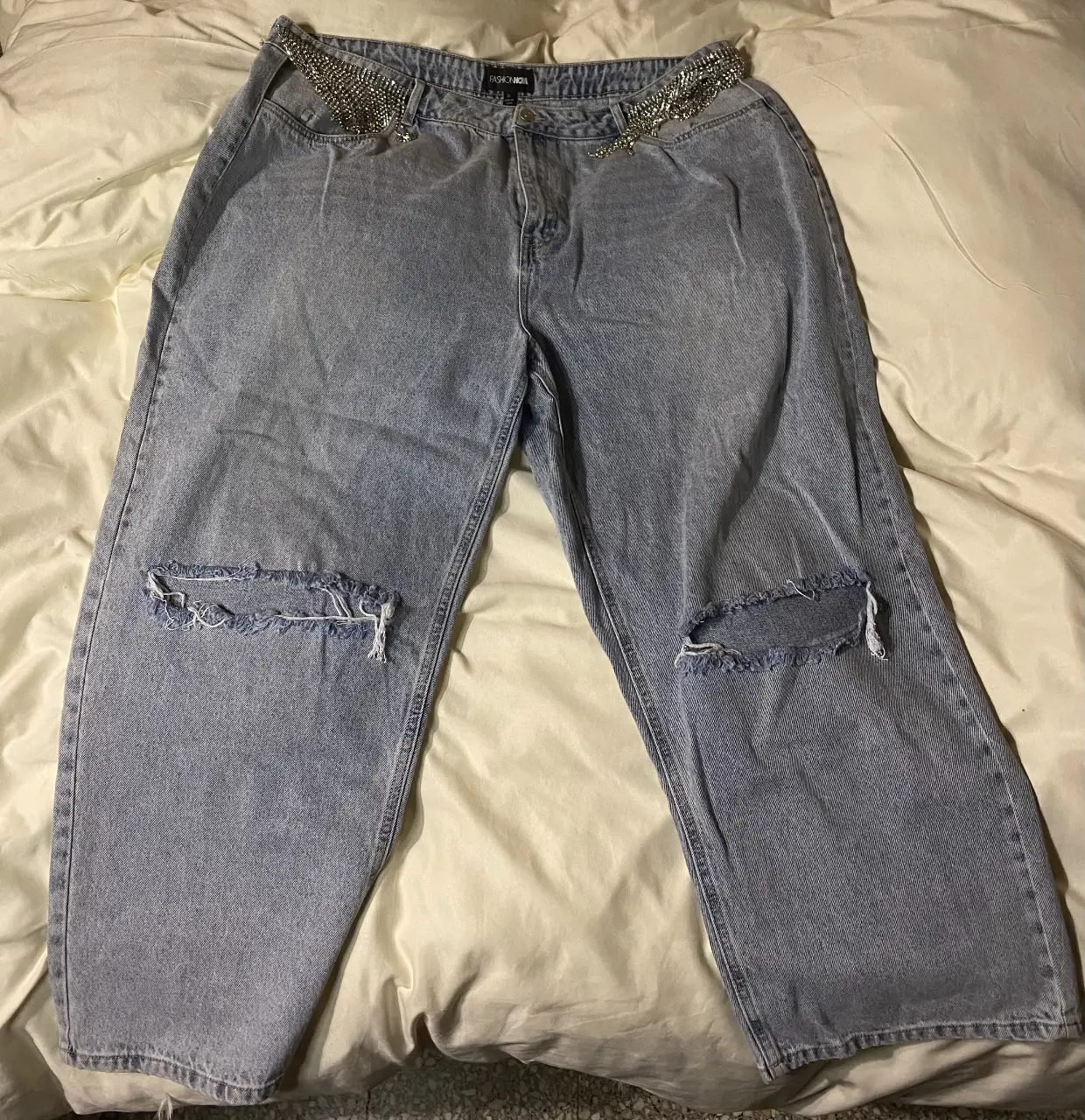 Jeans de mujer tiro alto, con roturas en las rodillas y detalles de strass en la cintura. Corte ancho y estilo Y2K. 