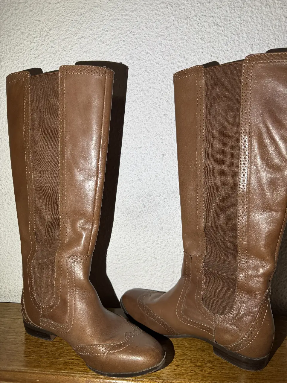 Botas de caña alta de cuero marrón, con detalles de diseño en el frente y elástico en los laterales. Suela con relieve y talle 36.