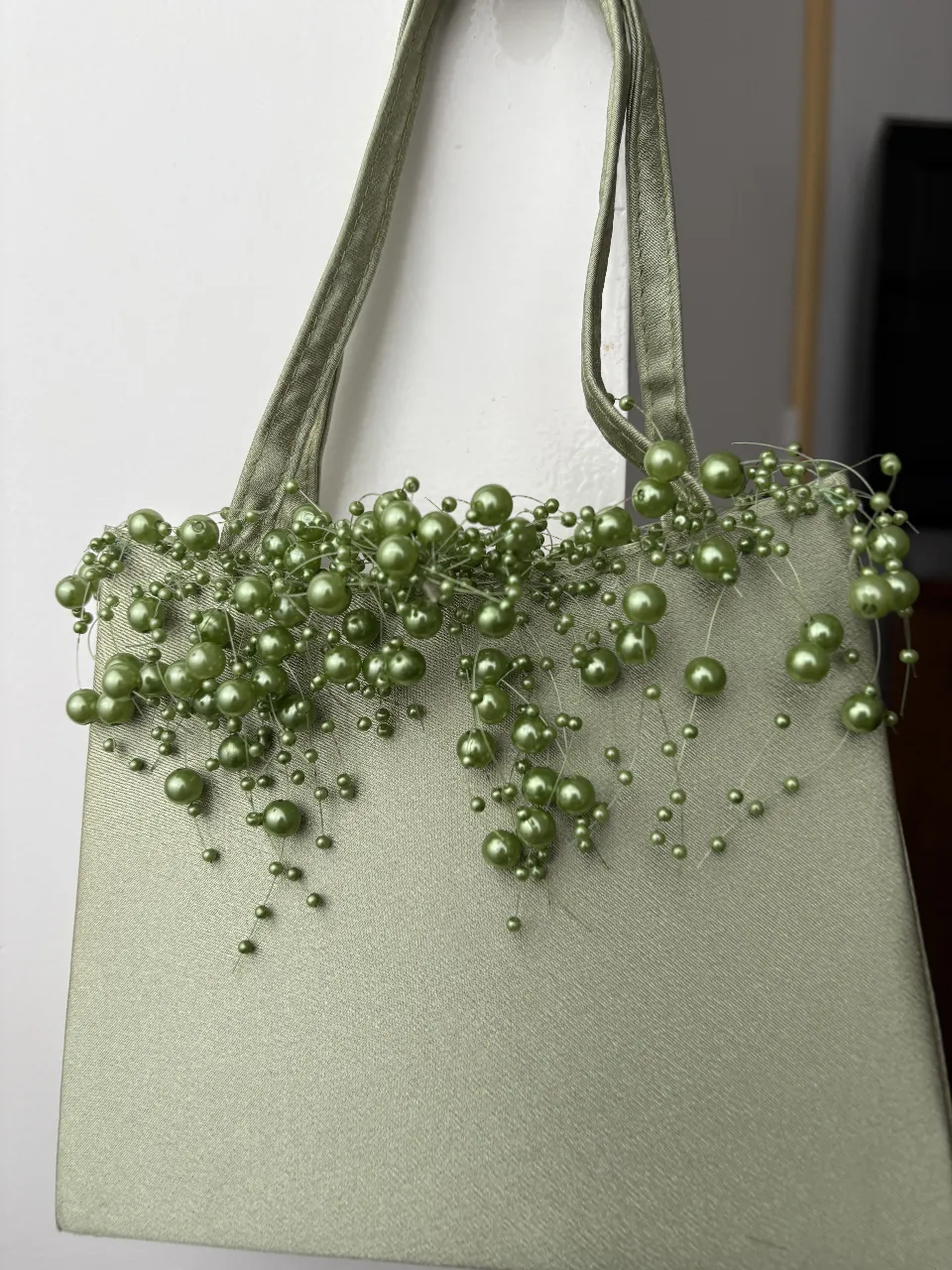 Carterita de seda de mano o de hombro, color verde agua, con delicados apliques de perlas y cuentas que le dan un toque súper chic y femenino. Ideal para complementar un look de fiesta o para darle un toque especial a un outfit más casual.