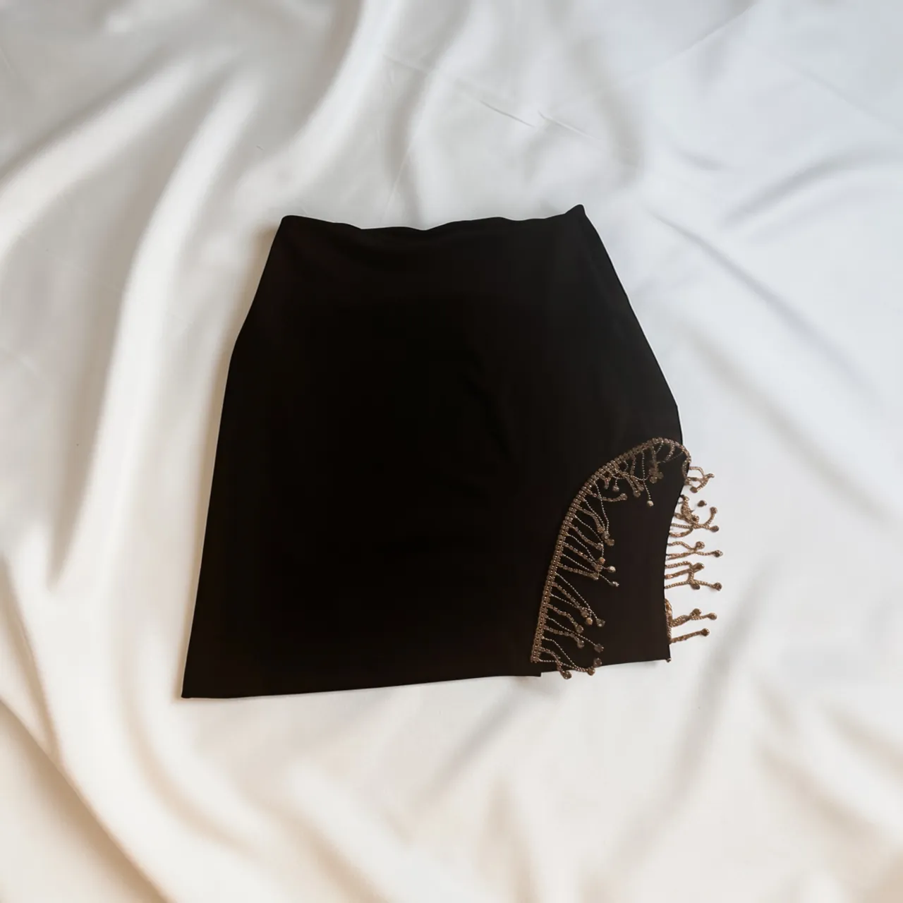 Pollera negra corta con detalles de strass y flecos dorados en un lateral. Diseño audaz y moderno, ideal para destacar en cualquier salida nocturna o evento especial.