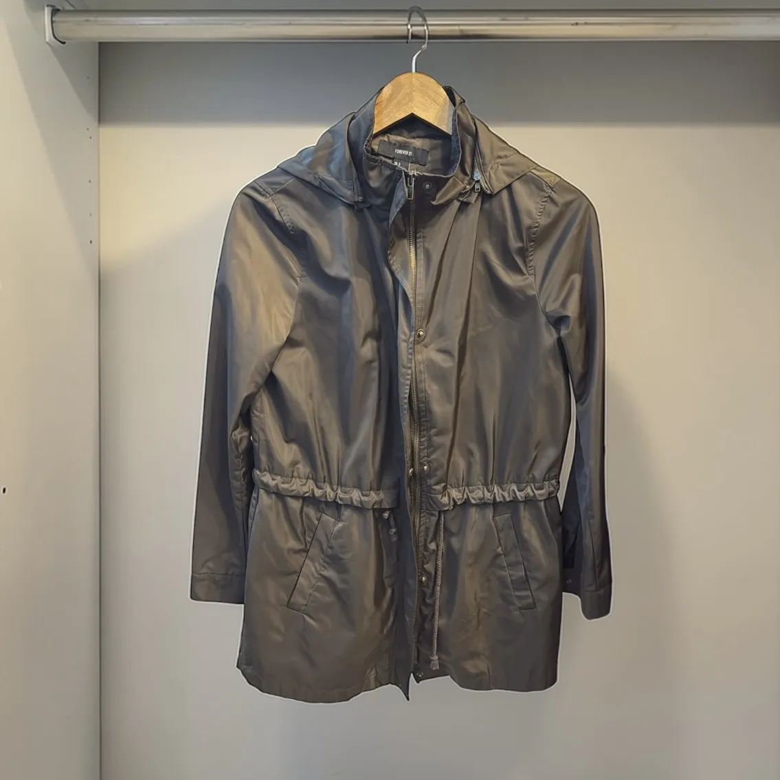 Campera impermeable gris con capucha y cordón de ajuste en la cintura. Cierre al frente y bolsillos laterales.