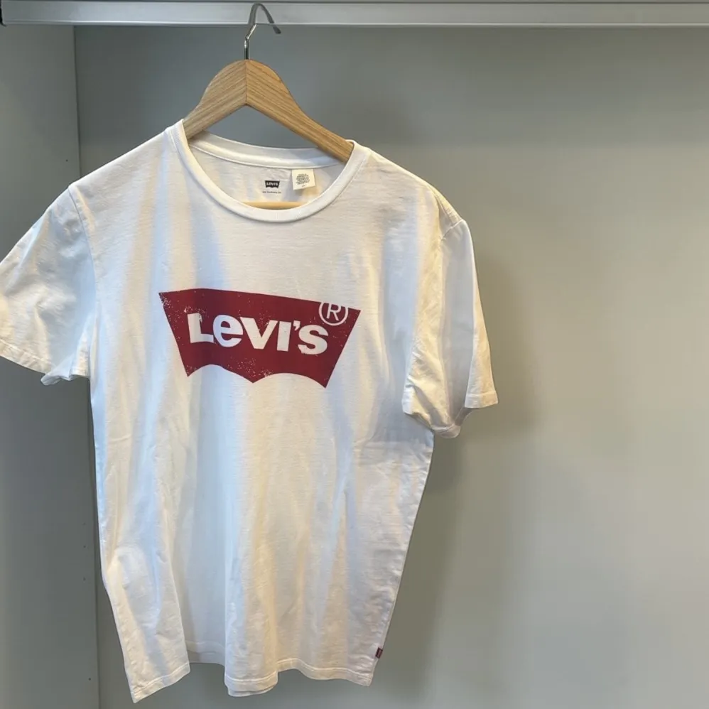 Remera blanca de manga corta con logo grande de Levi's en rojo en el frente, la parte gastada en el logo es parte de la remera