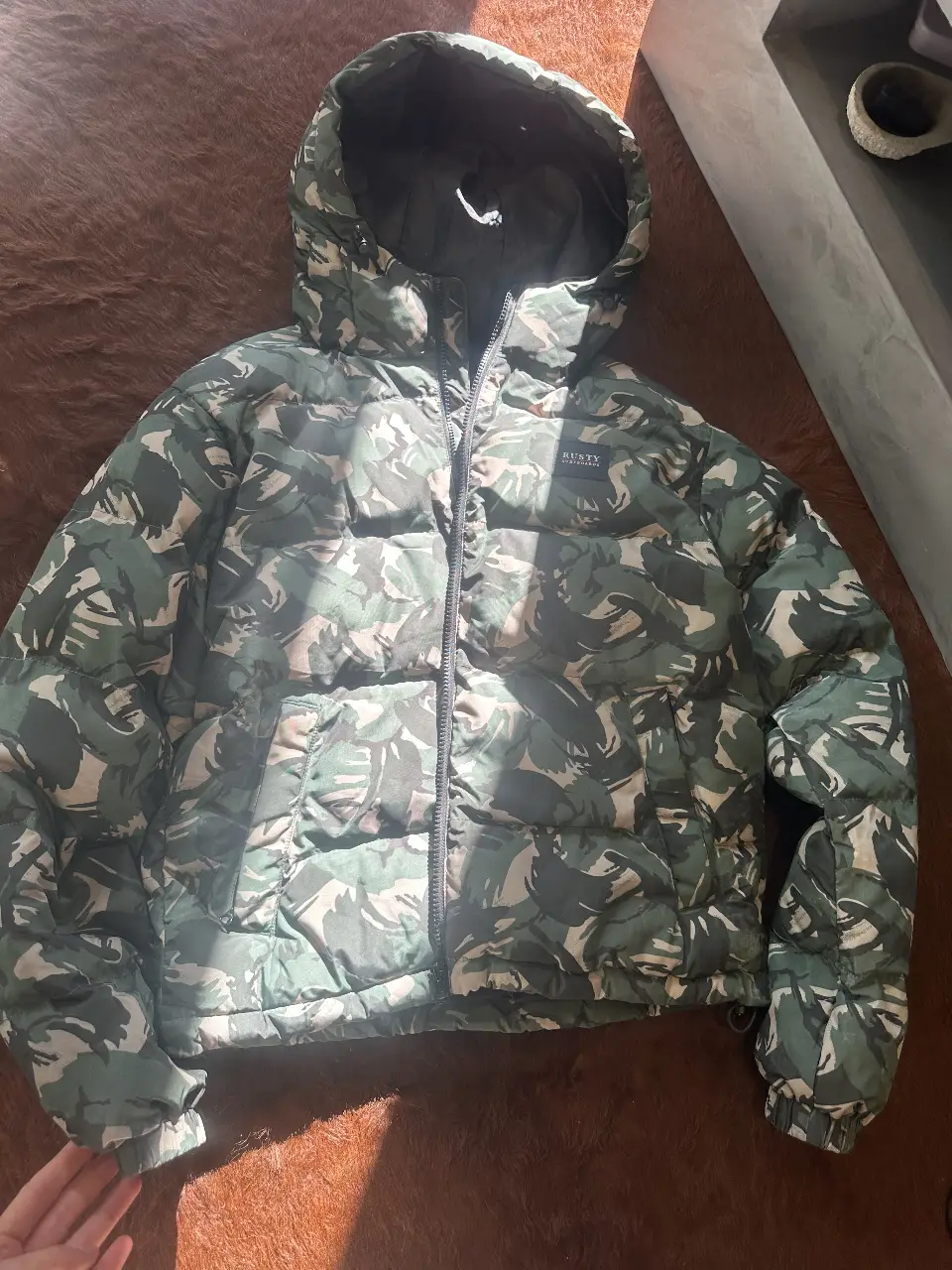 Campera de pluma RUSTY con estampado camuflado en tonos verdes y marrones. Ideal para el invierno, con capucha y cierre frontal. Campera de Nieve a la cadera. Talle M.