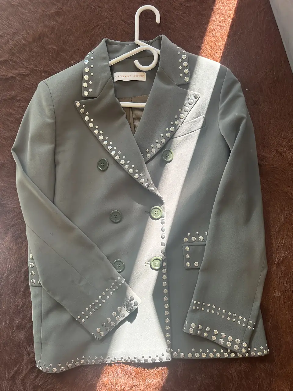 Elegante blazer de mujer color verde oliva con detalles de tachas plateadas. Perfecto para un look sofisticado y moderno. Marca Ginebra Privé.