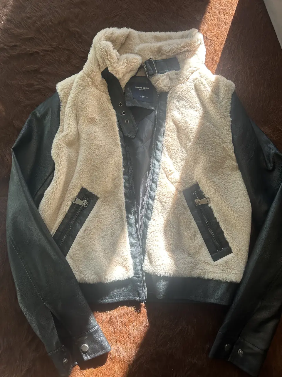 Campera biker de mujer con mangas negras de cuero sintético y cuerpo de piel sintética color crudo. Detalles de cierre y hebilla en el cuello. Ideal para un look casual y canchero.