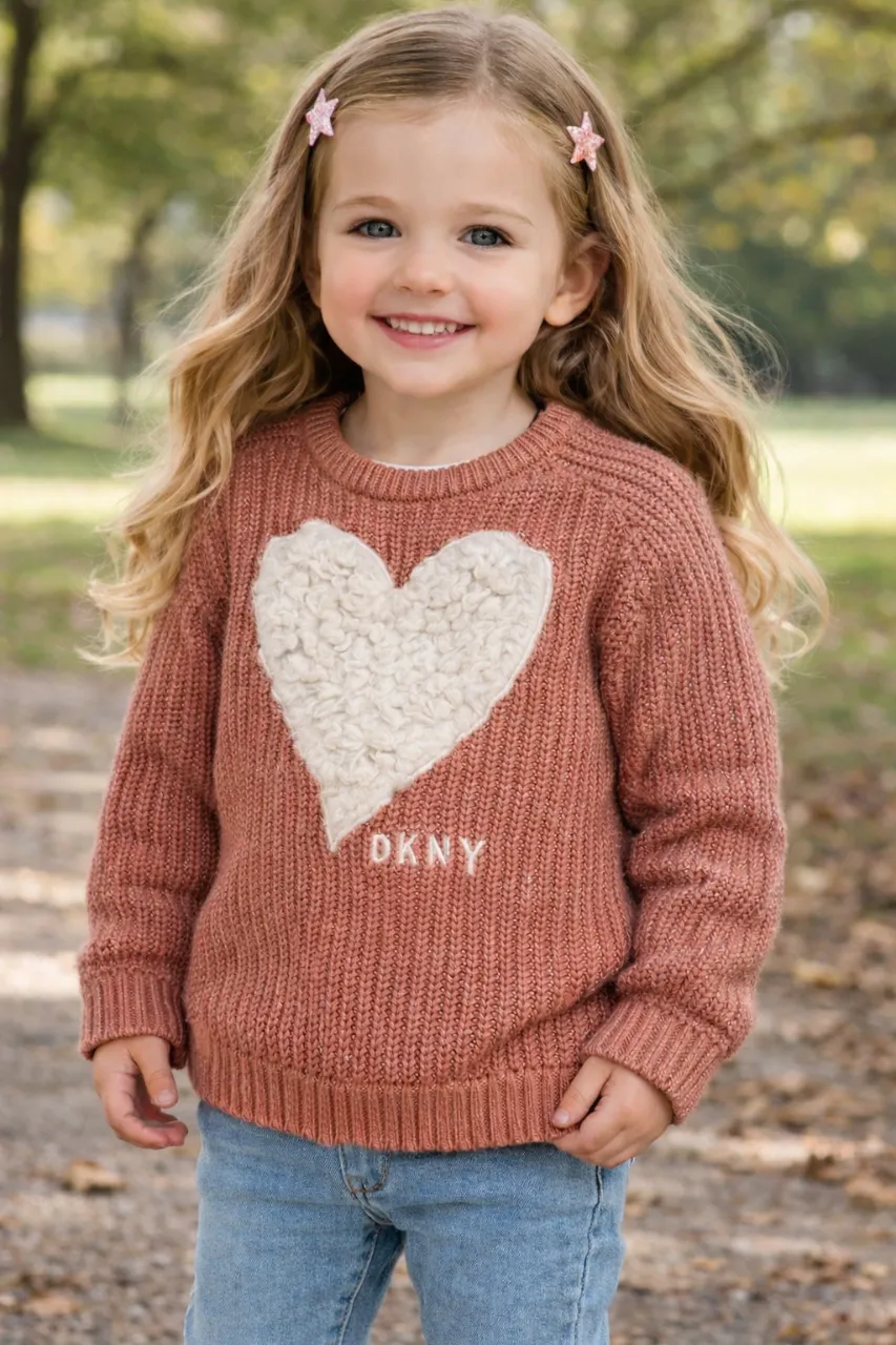 Sweater de lana tejido color salmón con un aplique de corazón blanco texturizado en el frente. Posee el logo de la marca bordado en blanco debajo del corazón. Cuello redondo y mangas largas.